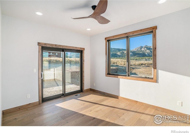 empty room with ceiling fan, a mountain view, light wood-type flooring, and plenty of natural light