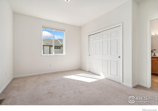 unfurnished bedroom with light carpet, a closet, and ensuite bathroom