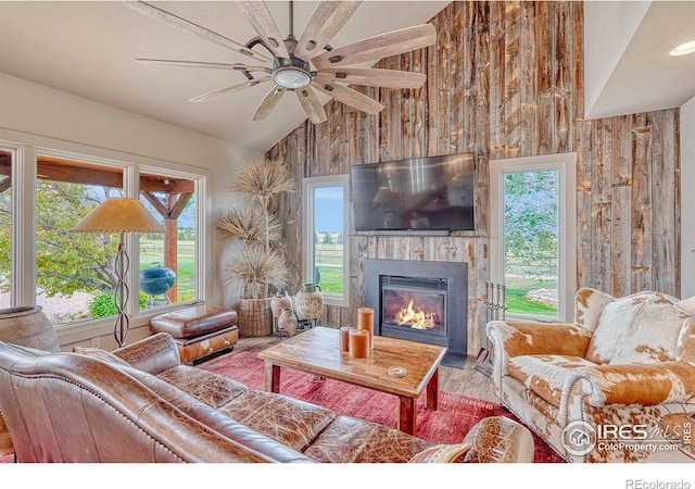 living room featuring ceiling fan, hardwood / wood-style flooring, wooden walls, and plenty of natural light