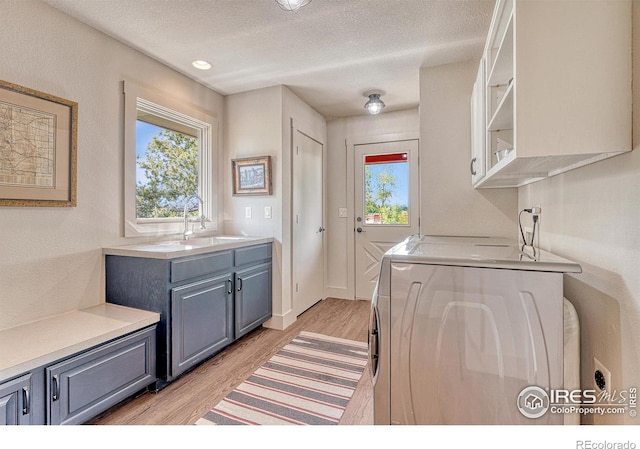 washroom with washer / clothes dryer, cabinets, light hardwood / wood-style floors, and sink