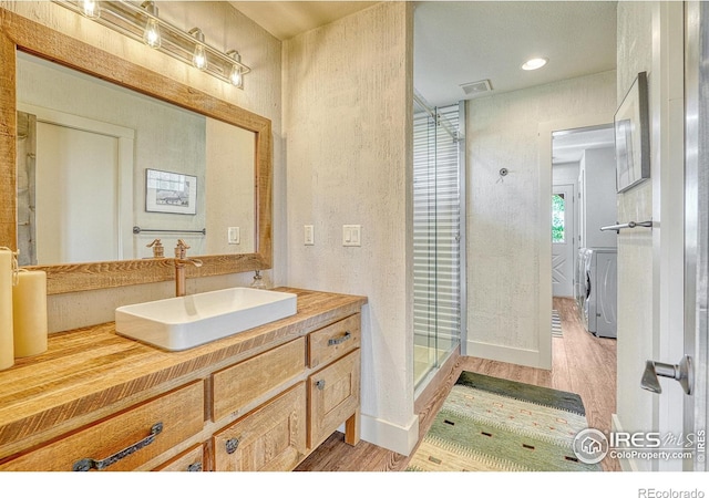 bathroom with a shower with door, hardwood / wood-style floors, vanity, and washer and clothes dryer