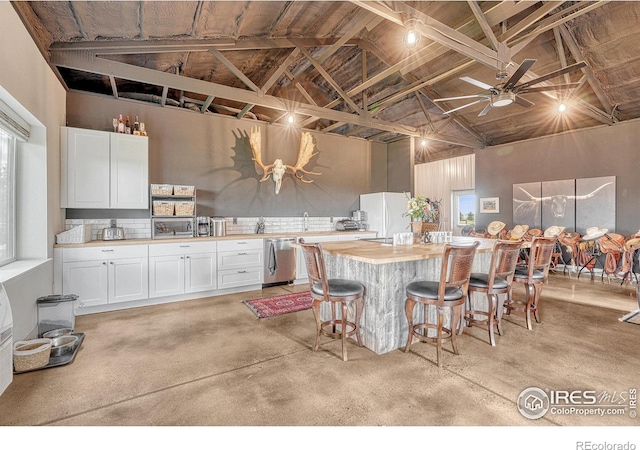 kitchen with ceiling fan, white cabinets, wooden counters, high vaulted ceiling, and a kitchen bar