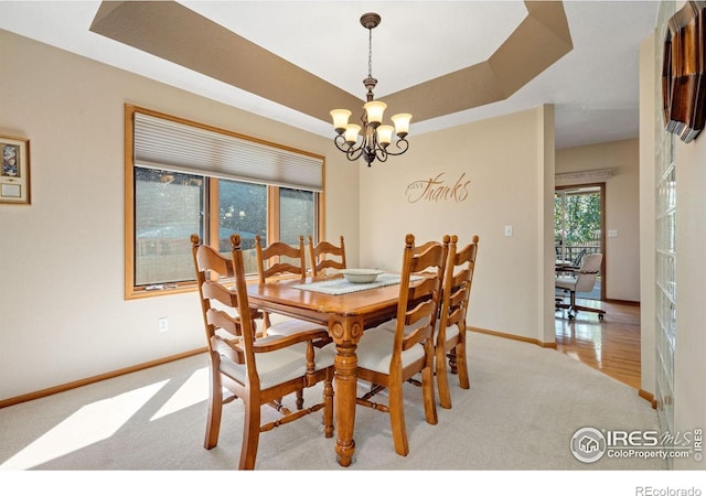 carpeted dining room with a raised ceiling and a chandelier