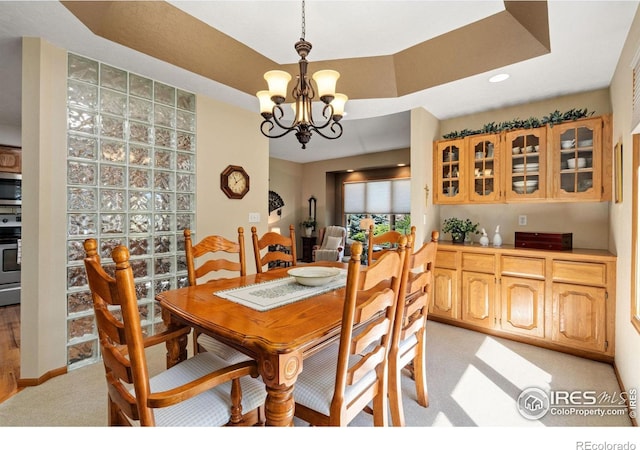 carpeted dining room featuring a notable chandelier and a raised ceiling