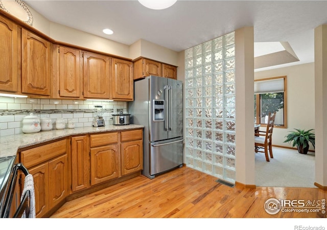 kitchen with tasteful backsplash, light hardwood / wood-style flooring, stainless steel appliances, and light stone counters