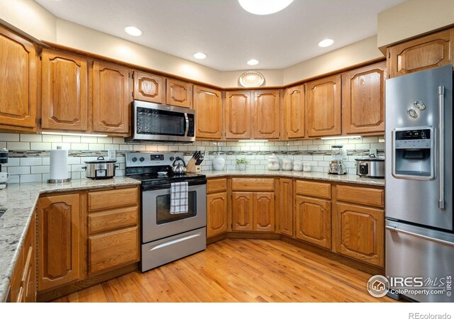 kitchen with stainless steel appliances, backsplash, light hardwood / wood-style floors, and light stone counters