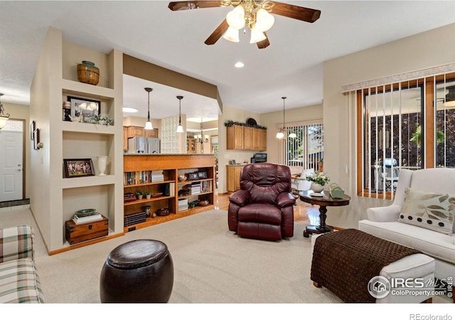 living room featuring ceiling fan with notable chandelier, built in shelves, and light carpet