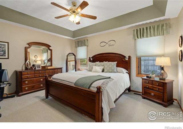 carpeted bedroom featuring ceiling fan, a raised ceiling, and multiple windows