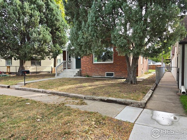 view of property hidden behind natural elements featuring brick siding and a gate