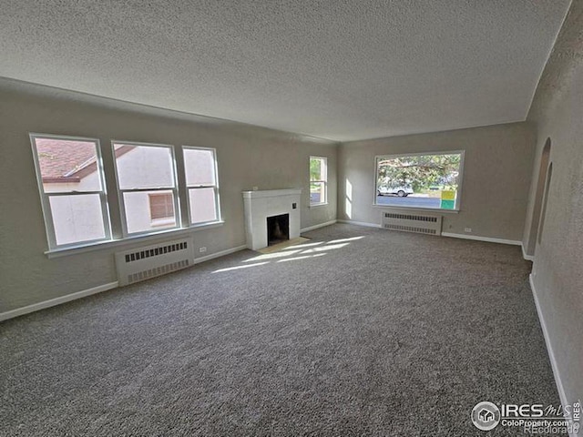 unfurnished living room featuring a textured ceiling, radiator, a fireplace with flush hearth, baseboards, and a textured wall