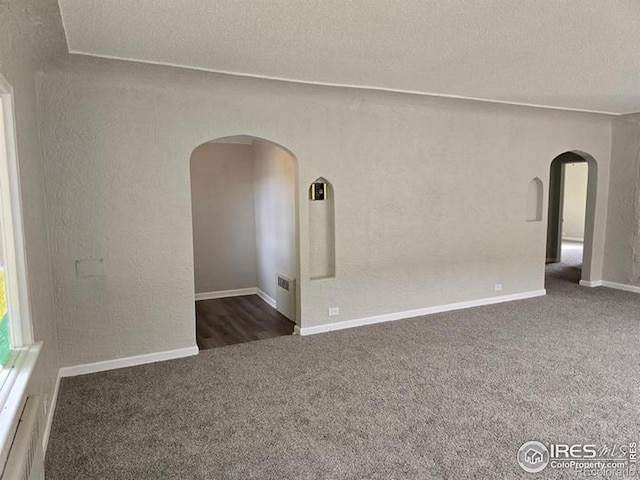 empty room featuring arched walkways, carpet, a textured ceiling, and baseboards