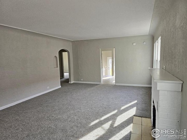 unfurnished living room featuring arched walkways, a textured wall, carpet, a fireplace with flush hearth, and baseboards