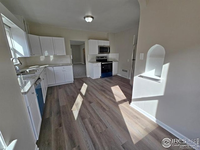kitchen with appliances with stainless steel finishes, a sink, dark wood-style floors, white cabinets, and arched walkways
