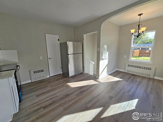 unfurnished dining area featuring radiator heating unit, arched walkways, a chandelier, dark wood-style floors, and baseboards