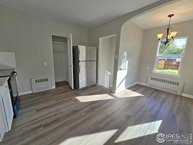 unfurnished dining area with radiator, arched walkways, a chandelier, and dark wood-type flooring