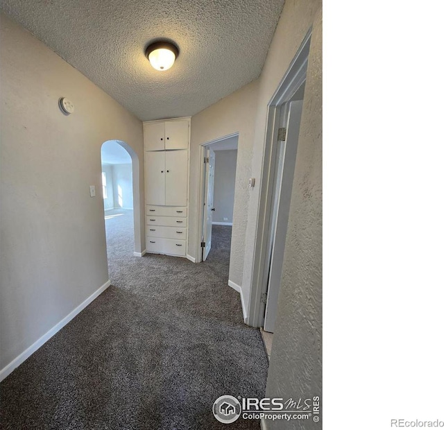 hallway with arched walkways, carpet floors, a textured ceiling, and baseboards