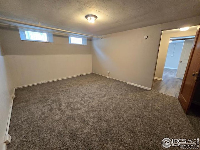 basement featuring dark colored carpet, a textured ceiling, and baseboards