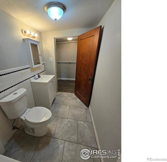 bathroom with toilet, vanity, tile patterned flooring, a textured ceiling, and tile walls