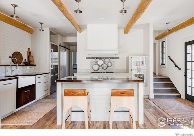 kitchen with light wood-type flooring, beam ceiling, and a kitchen bar