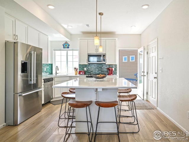 kitchen featuring pendant lighting, light hardwood / wood-style flooring, white cabinetry, appliances with stainless steel finishes, and a center island