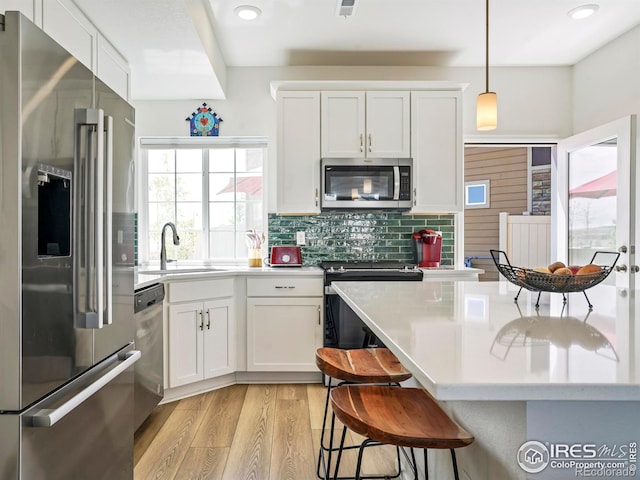 kitchen featuring white cabinets, stainless steel appliances, light wood-type flooring, decorative light fixtures, and sink