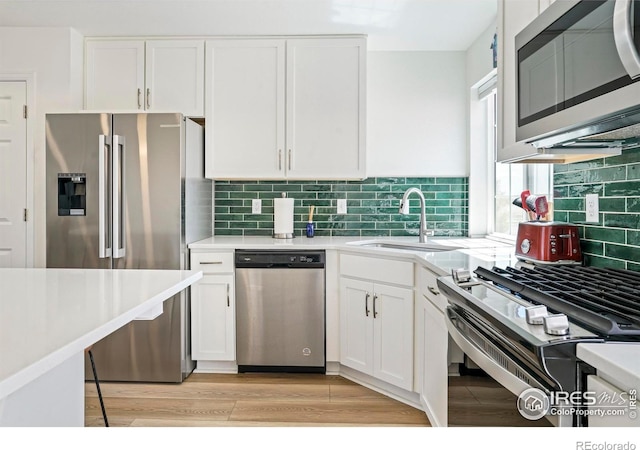 kitchen with stainless steel appliances, backsplash, light hardwood / wood-style floors, and white cabinetry