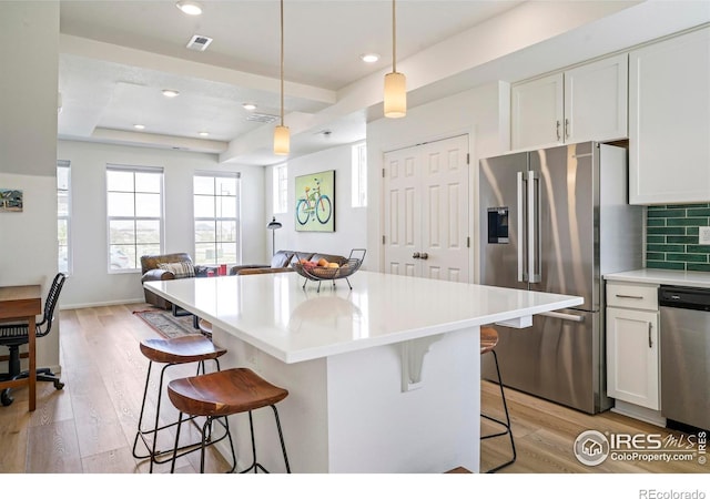 kitchen featuring white cabinets, pendant lighting, appliances with stainless steel finishes, a tray ceiling, and a breakfast bar