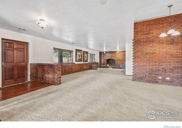 unfurnished living room with a textured ceiling, brick wall, a fireplace, and carpet flooring