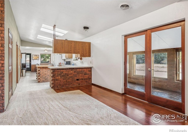 kitchen with french doors, vaulted ceiling with skylight, dark hardwood / wood-style floors, and kitchen peninsula