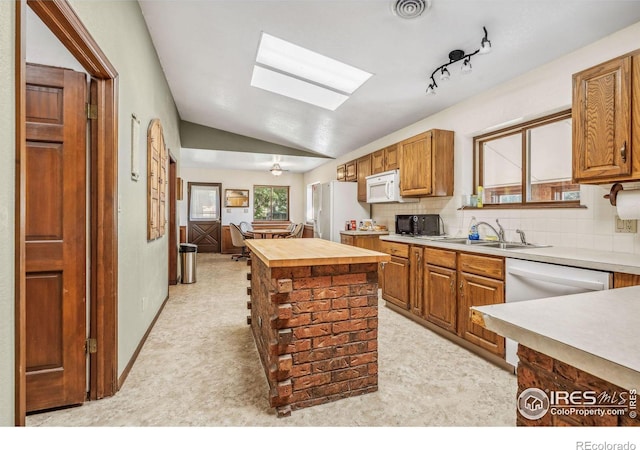 kitchen featuring decorative backsplash, white appliances, lofted ceiling, a center island, and sink