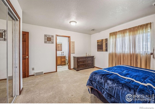 bedroom featuring light carpet, a closet, a textured ceiling, and ensuite bathroom