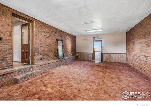 unfurnished living room featuring a textured ceiling, carpet, wooden walls, and brick wall