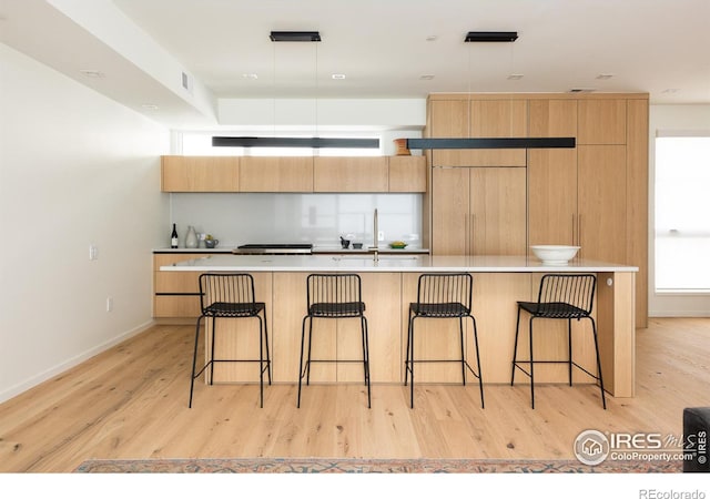 kitchen with decorative light fixtures, light wood-type flooring, a kitchen bar, and a kitchen island