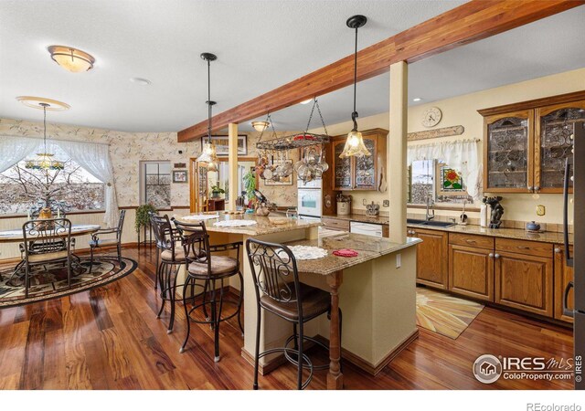 kitchen with wallpapered walls, brown cabinetry, a kitchen island, glass insert cabinets, and a breakfast bar