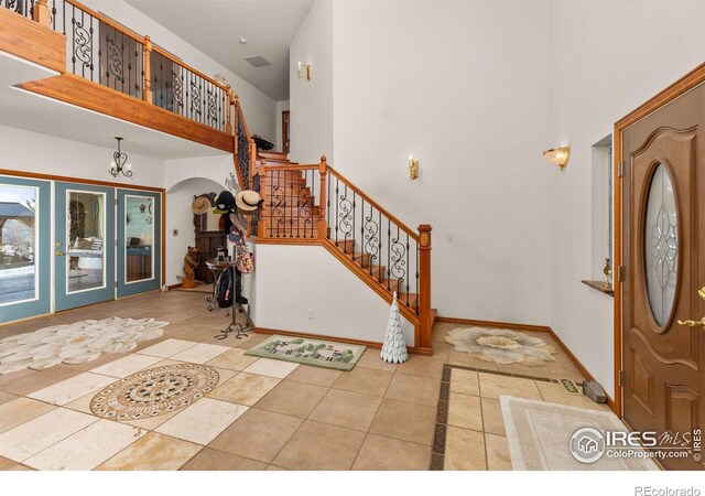 tiled entrance foyer with arched walkways, a towering ceiling, baseboards, stairway, and an inviting chandelier