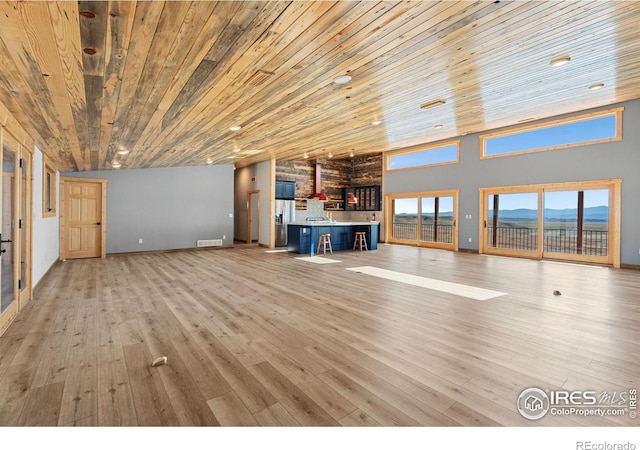 unfurnished living room with wooden ceiling, light hardwood / wood-style floors, a mountain view, and high vaulted ceiling