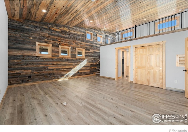 unfurnished living room featuring wooden walls, hardwood / wood-style flooring, a high ceiling, and wooden ceiling