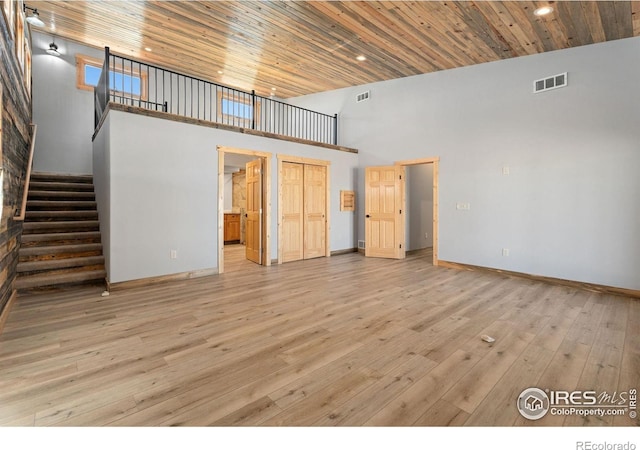 unfurnished living room featuring a towering ceiling, wooden ceiling, and light wood-type flooring