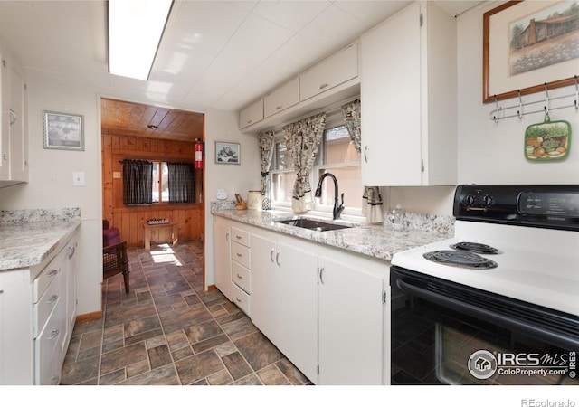 kitchen with white electric range oven, wooden walls, sink, and white cabinets