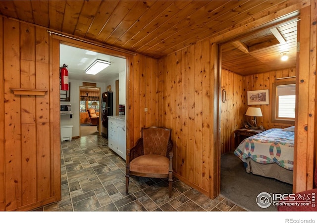 bedroom with wood walls, black refrigerator, and wood ceiling