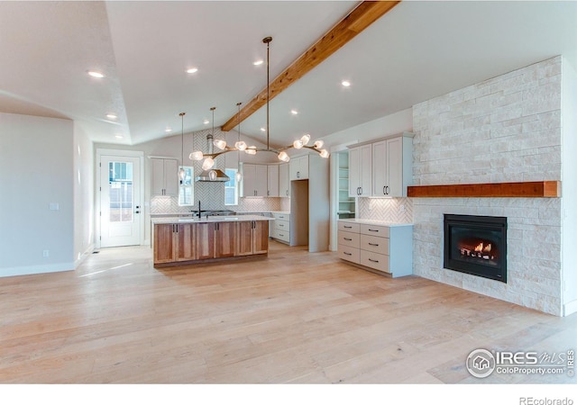 kitchen featuring an island with sink, light wood-style flooring, tasteful backsplash, light countertops, and vaulted ceiling with beams