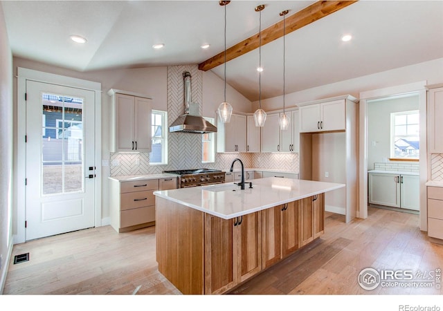 kitchen featuring wall chimney range hood, range with two ovens, white cabinets, and a center island with sink