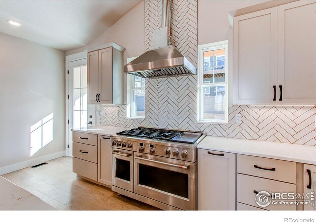 kitchen with double oven range, visible vents, baseboards, wall chimney exhaust hood, and tasteful backsplash