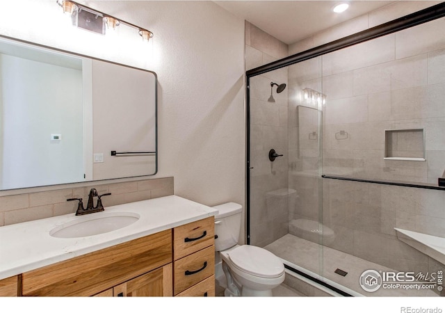 bathroom with vanity, toilet, a shower stall, and tasteful backsplash