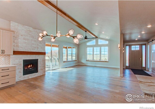 entrance foyer featuring ceiling fan with notable chandelier, lofted ceiling with beams, a fireplace, light wood finished floors, and baseboards