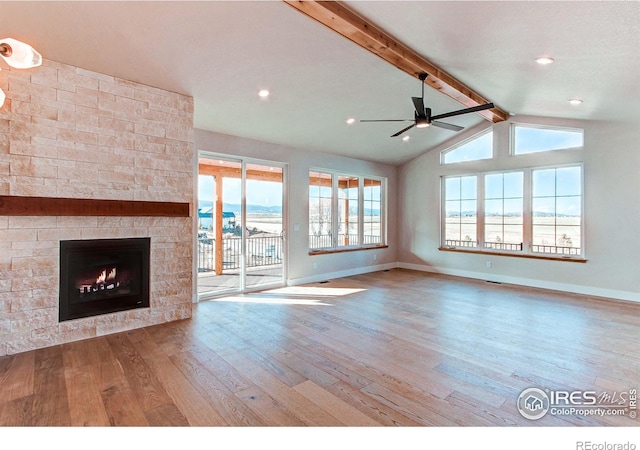 unfurnished living room featuring baseboards, lofted ceiling with beams, a stone fireplace, a ceiling fan, and wood-type flooring