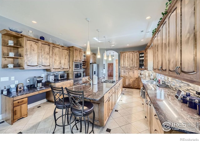 kitchen featuring an island with sink, decorative light fixtures, stainless steel appliances, a kitchen breakfast bar, and dark stone countertops