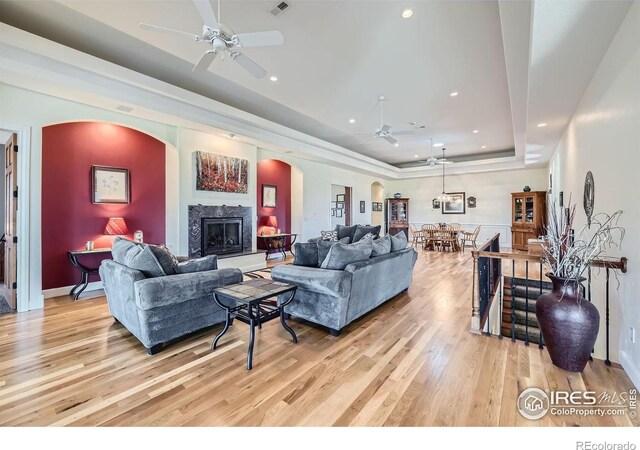 living room featuring a premium fireplace, ceiling fan, light hardwood / wood-style flooring, and a raised ceiling