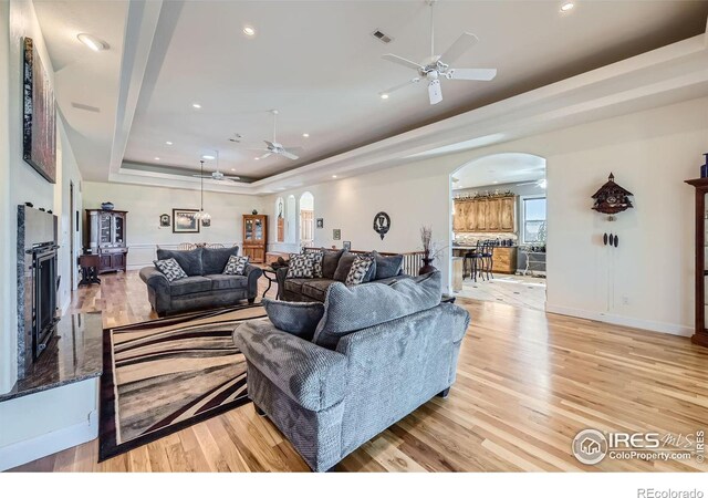 living room with ceiling fan, a tray ceiling, and light hardwood / wood-style flooring