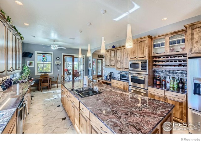 kitchen featuring a kitchen island, ceiling fan, stainless steel appliances, dark stone countertops, and decorative light fixtures